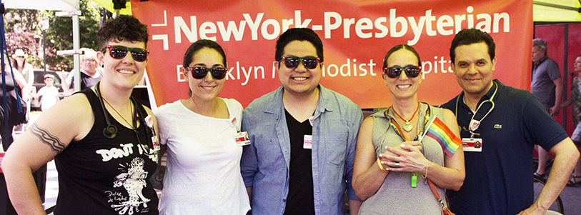 A group of people posing for a photo in front of a NewYork-Presbyterian sign at the pride parade 