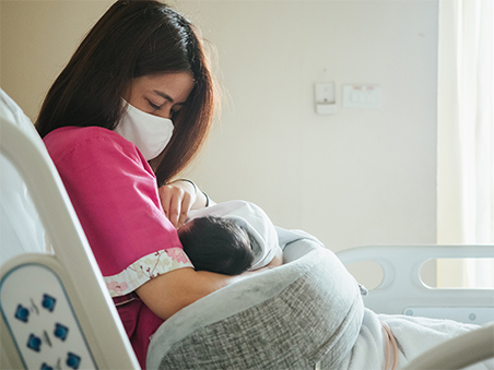 images of mom in mask holding baby in hospital bed