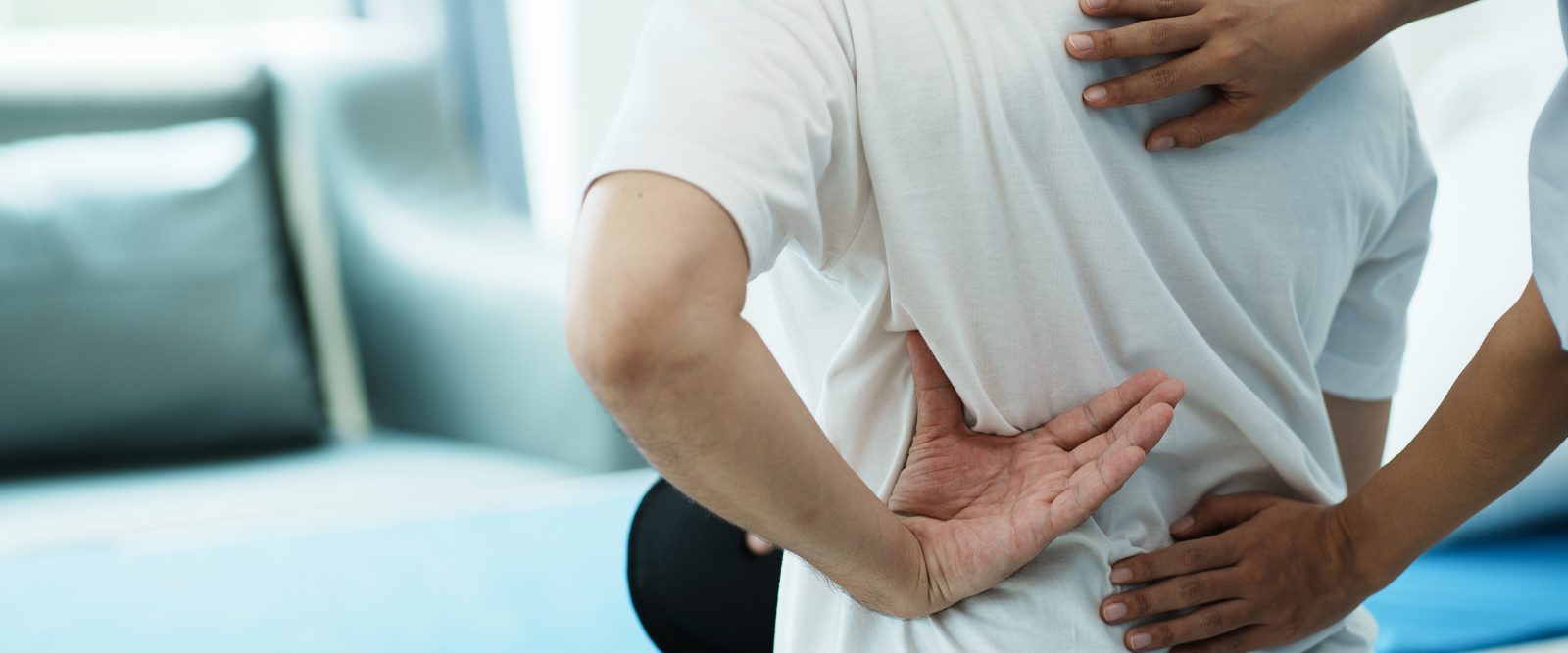 A man holding a hand to his back while a doctor examines them.