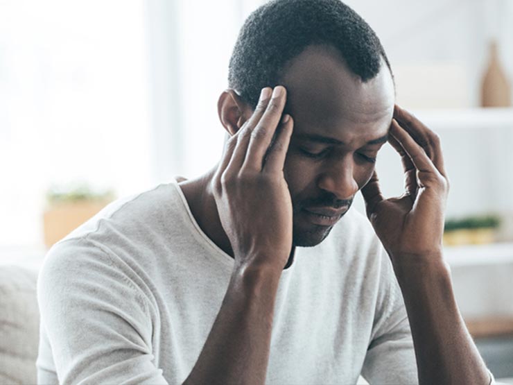 African American man with migraine headache holds his head.