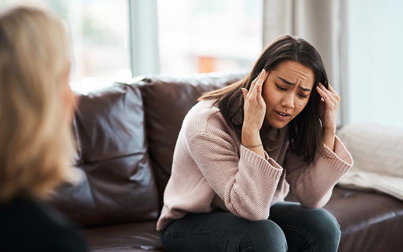 A woman sitting on a couch holding her head