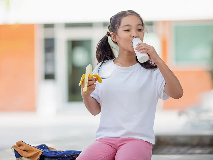 image of girl holding banana and drinking milk