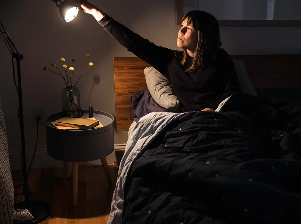 Young woman turning bedside light off.