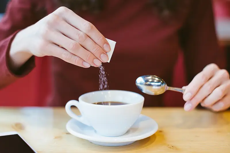 image of person pouring sugar packet into cup of coffee